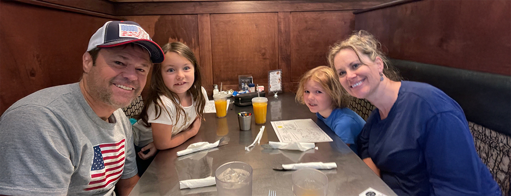 Image of Justin Osmond and his two daughters and wife sitting in a restaurant booth